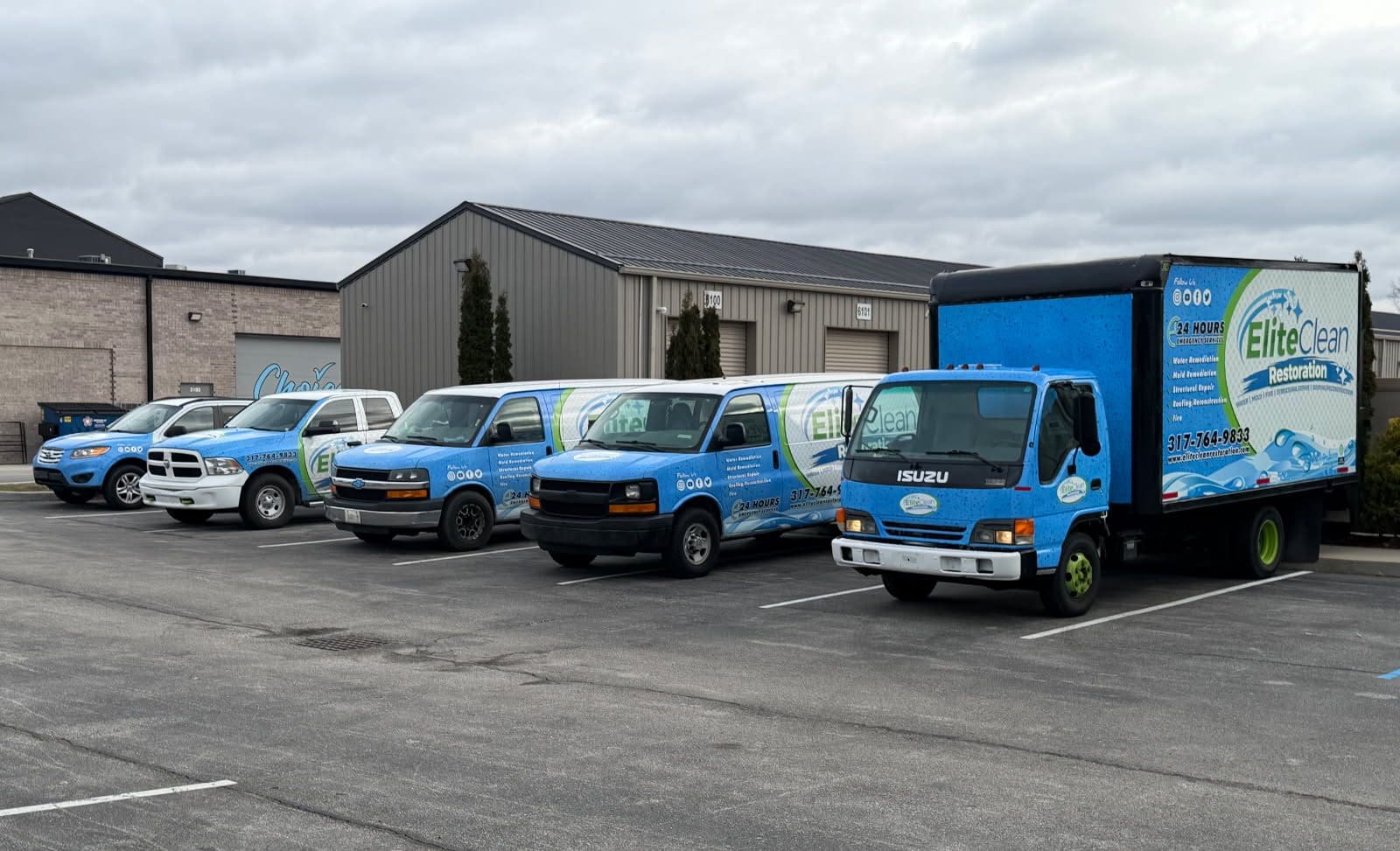 Five Elite Clean service vehicles, including vans, a box truck, and a pickup truck, are parked in a row in a parking lot outside a commercial building on a cloudy day.