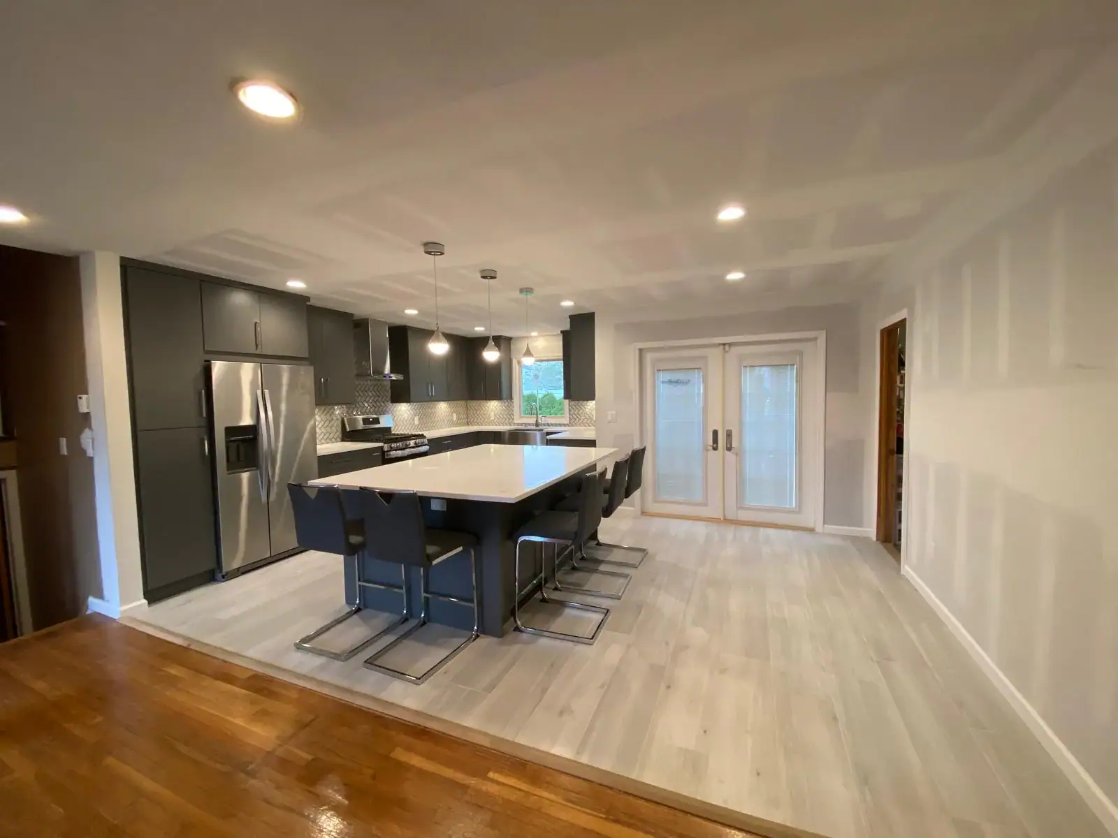 Modern kitchen with gray cabinets, stainless steel appliances, a large white island with six black chairs, light wood flooring, recessed lighting, and double glass doors—expertly restored by Water Damage Restoration Indiana.