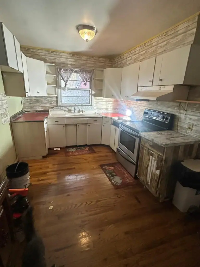 A kitchen with wooden floors, white cabinets, a stainless steel stove, and a double sink under a window with curtains. The rustic countertops and backsplash reflect the charm you'd expect after expert Water Damage Restoration Indiana services.
