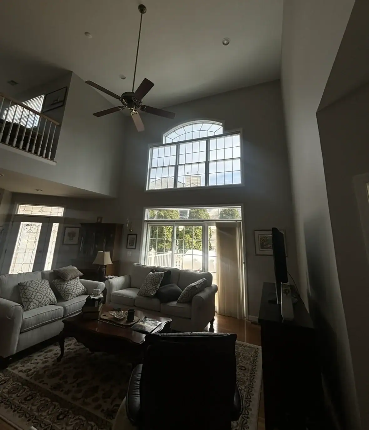A spacious living room with high ceilings and large windows letting in natural light, gray sofas, a wooden coffee table, and a patterned rug. Water Damage Restoration Indiana services can help maintain this inviting space in top condition.