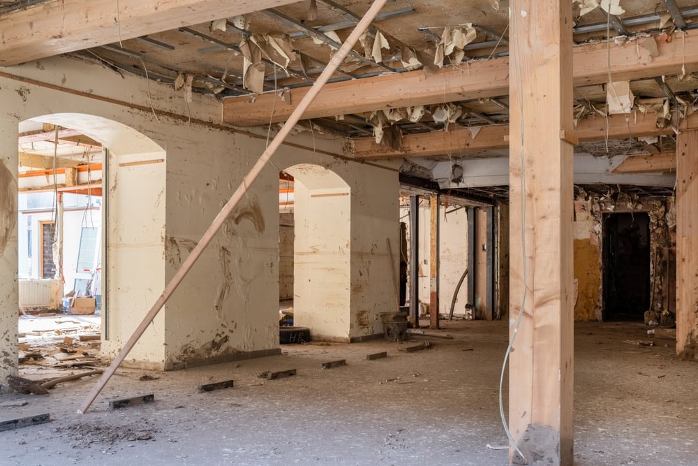 An abandoned building interior with exposed beams, unfinished walls, and debris scattered on the dusty floor shows clear signs of neglect—an ideal candidate for Water Damage Restoration Indiana experts to revive. Natural light enters through arched doorways.