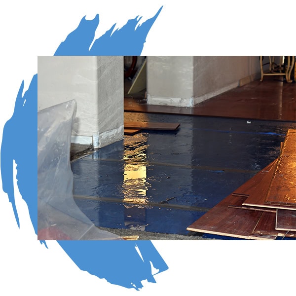 A floor with water damage is shown, with water pooling on a blue surface and pieces of wooden flooring pulled up. Plastic sheeting is partially visible, suggesting recent flooding—a scene in need of Water Damage Restoration Indiana experts.