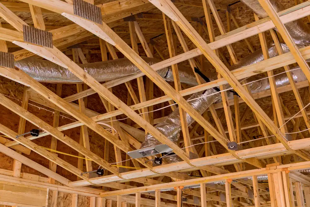 Wooden framing and trusses of a building under construction with exposed HVAC ductwork and electrical wiring visible on the ceiling.