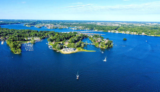 Aerial view of a Marion County lake with boats, green islands, and forested shoreline under blue sky.