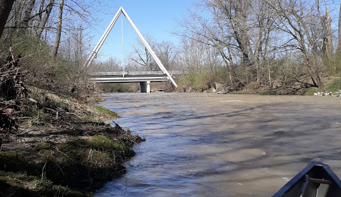 A muddy river flows beneath a white triangular bridge near leafless trees in Hamilton County.