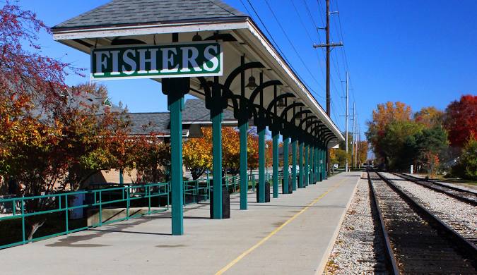 A train station platform labeled "Fishers" features green supports, trees, and local water damage services.