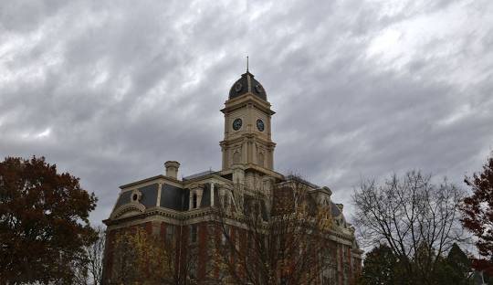 A historic courthouse with a clock tower stands under cloudy skies, framed by autumn trees in Hamilton County.